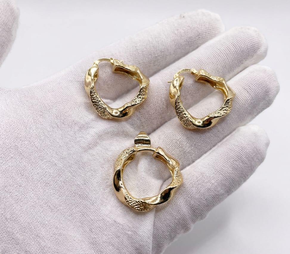 Three gold hoop earrings and pendant on a white glove