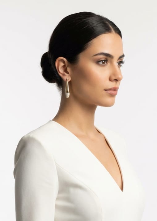 Woman wearing a white dress with a gold-plated earrings against a plain background