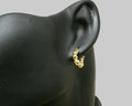 Gold-plated earring on a black mannequin ear against a neutral background