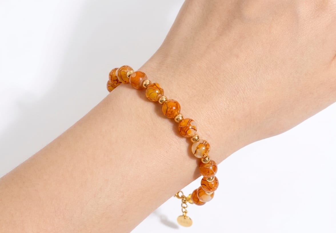 Beaded bracelet with orange beads on a wrist against a white background