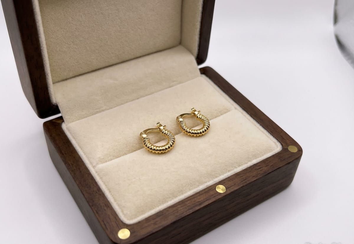 Gold hoop earrings in a wooden jewelry box on a white background