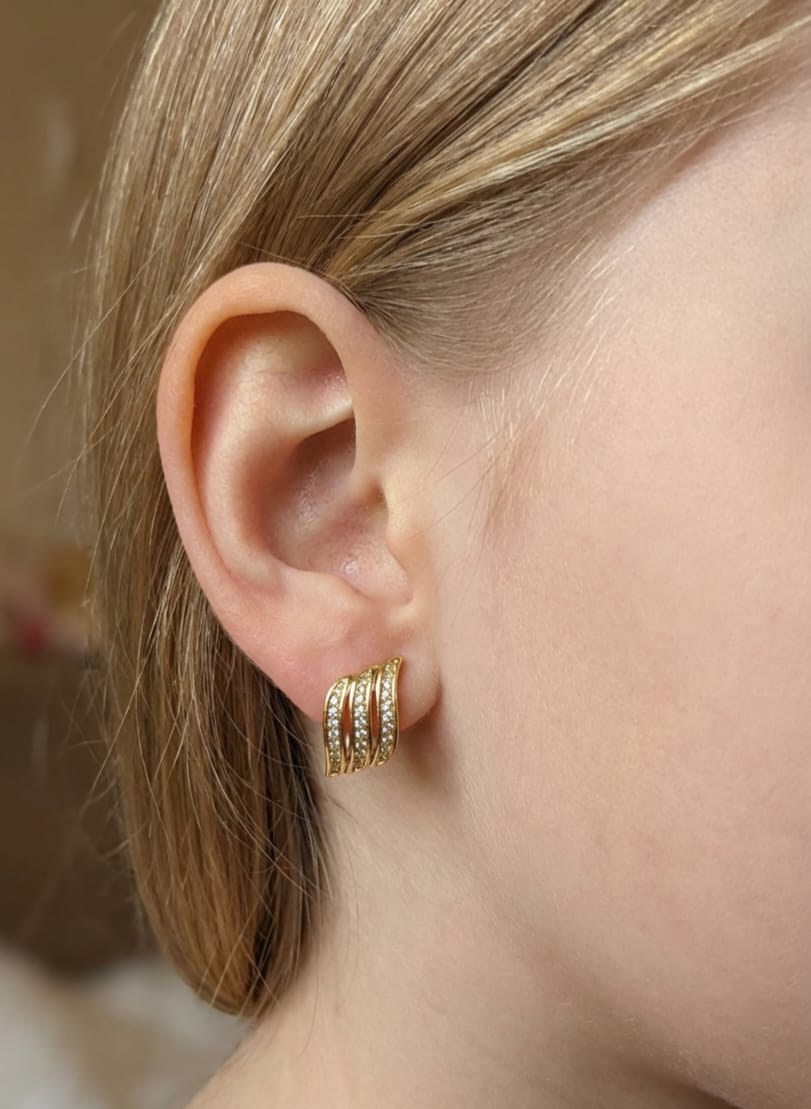 Close-up of a person wearing gold hoop earrings with a blurred background
