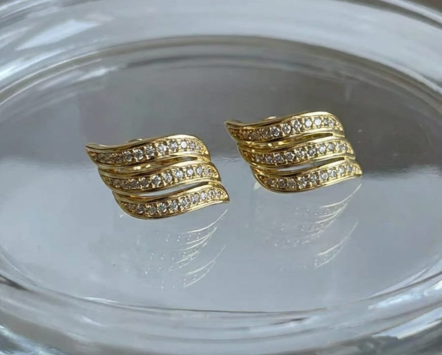 Gold-plated earrings on a clear glass surface.