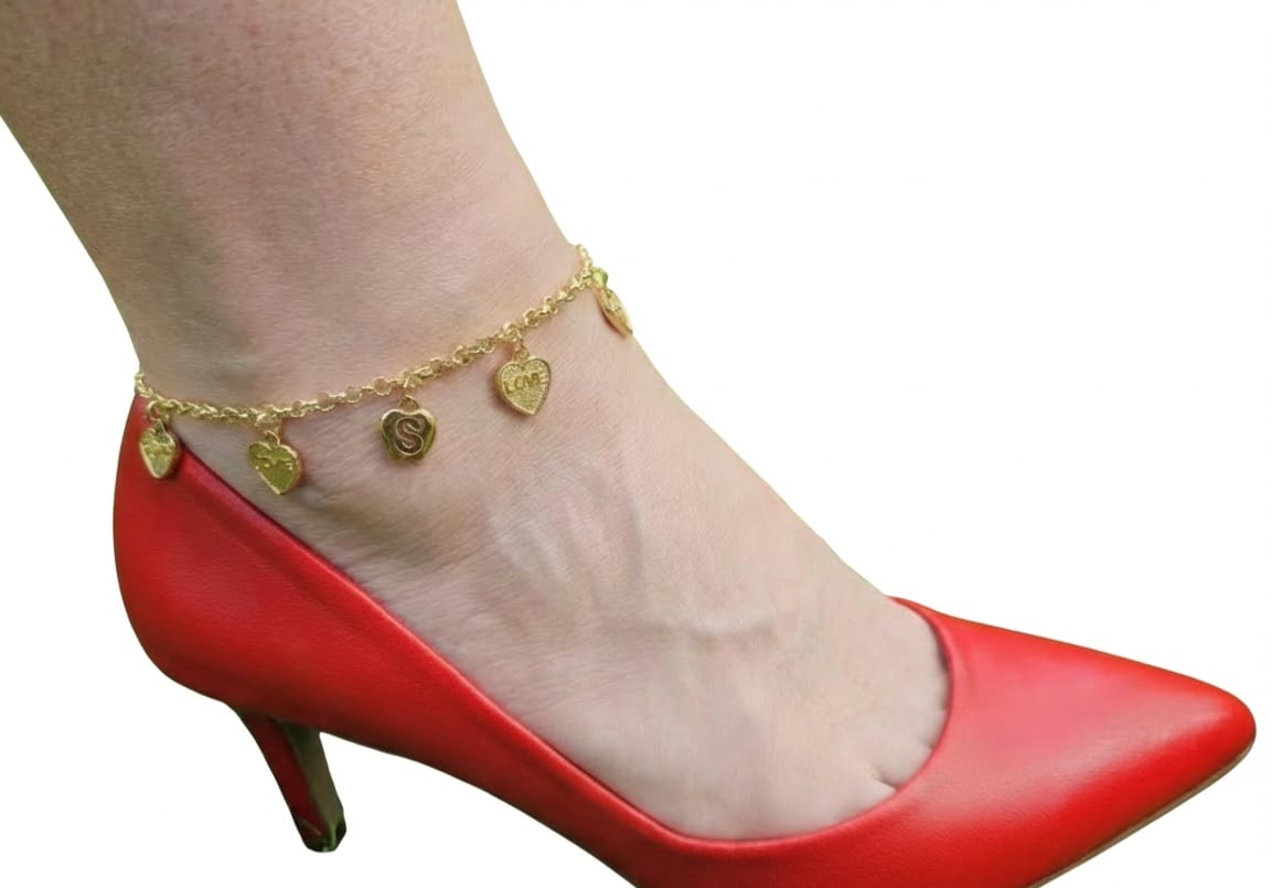 Gold anklet with heart charms on a foot wearing a red high-heeled shoe.