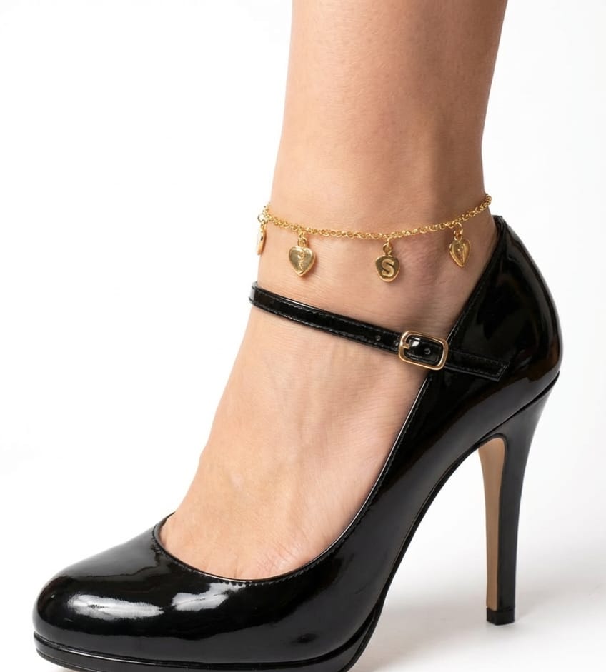 Black high-heeled shoe with a gold ankle strap and heart-shaped charms on a white background