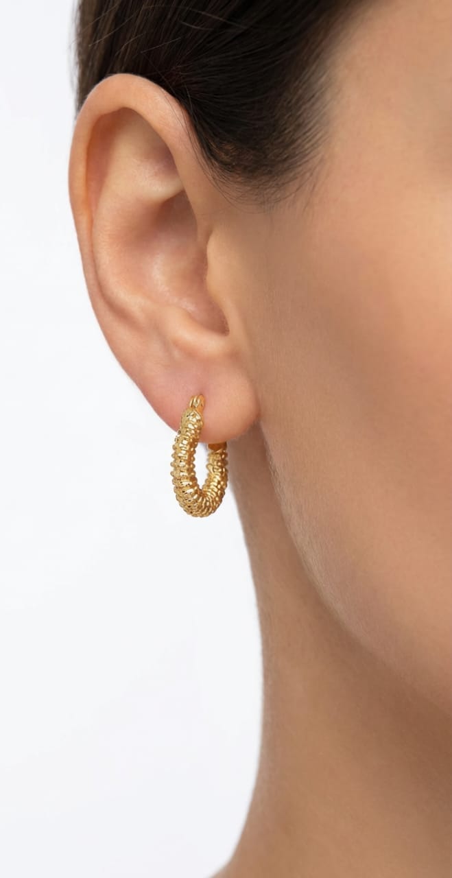 Gold hoop earring worn on a model's ear against a neutral background