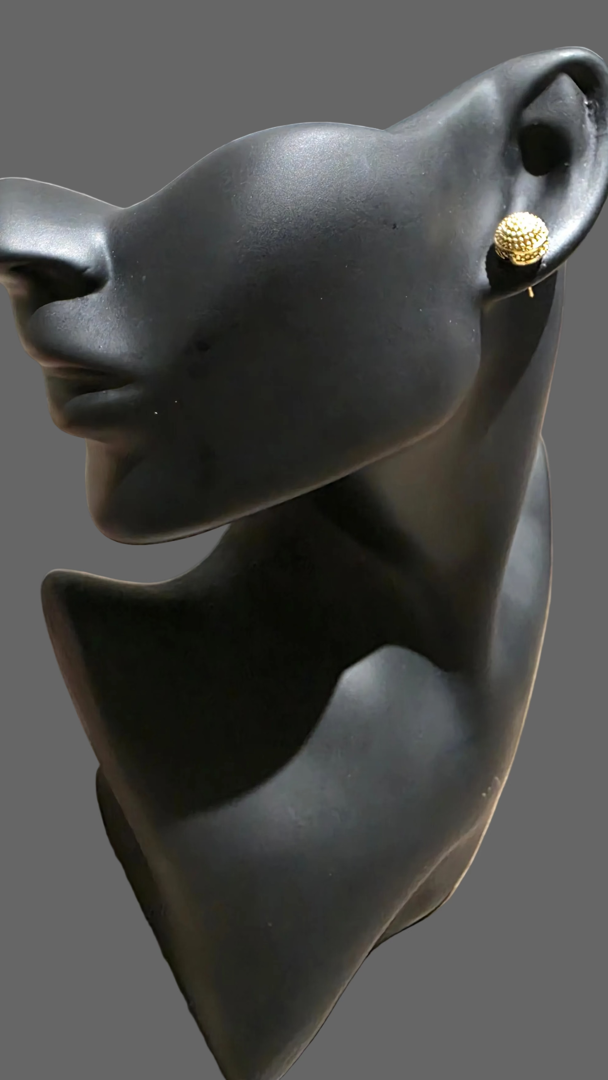 Black mannequin head with a gold earring on a wooden floor.
